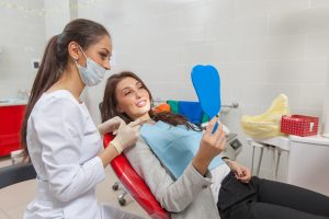 Woman sitting in the dentists chair looking in the mirror after her emergency dental care treatment.