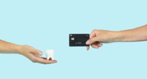 one hand holding credit card another holding model of a tooth